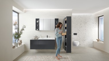 Vrouw opent hoge kast met veel opbergruimte in de badkamer met badkamermeubels uit de Geberit Acanto-serie.